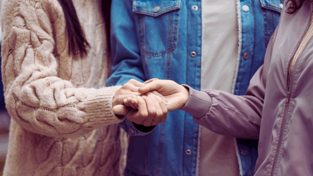 Hands held in emotional support between three people, symbolizing connection, trust, and relational healing in couples therapy intensives.